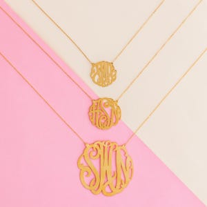 May include: Three gold necklaces with different sized circular pendants featuring monogrammed initials. The pendants are made of a delicate, openwork design.