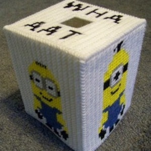 May include: A white tissue box cover with a yellow and blue Minion character on each side. The front of the box has the word "WHAT" written on it.