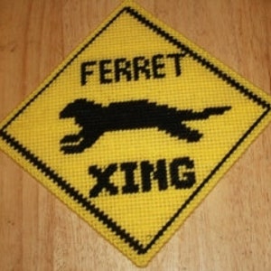 May include: A yellow diamond-shaped sign with black lettering and a black silhouette of a ferret running. The sign reads "FERRET XING".