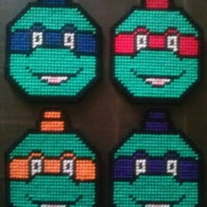 May include: Four handmade cross-stitch Teenage Mutant Ninja Turtles coasters. Each coaster features a different colored bandana: blue, red, orange, and purple.