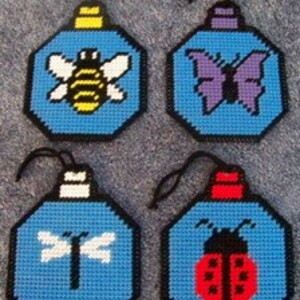May include: Four plastic canvas ornaments featuring different insects. The ornaments are blue with a white bee, a purple butterfly, a white dragonfly, and a red ladybug.