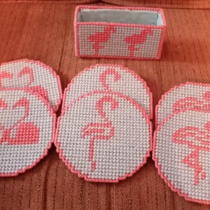May include: Set of six pink flamingo coasters with a white background. The coasters are made of plastic canvas and are perfect for adding a touch of whimsy to your home decor.