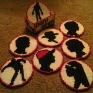 May include: Set of seven white and red crocheted coasters featuring black silhouette profiles of characters from the popular TV show 'Stranger Things'. The coasters are arranged in a circle around a small white box with the words 'Don't Open' printed on it.
