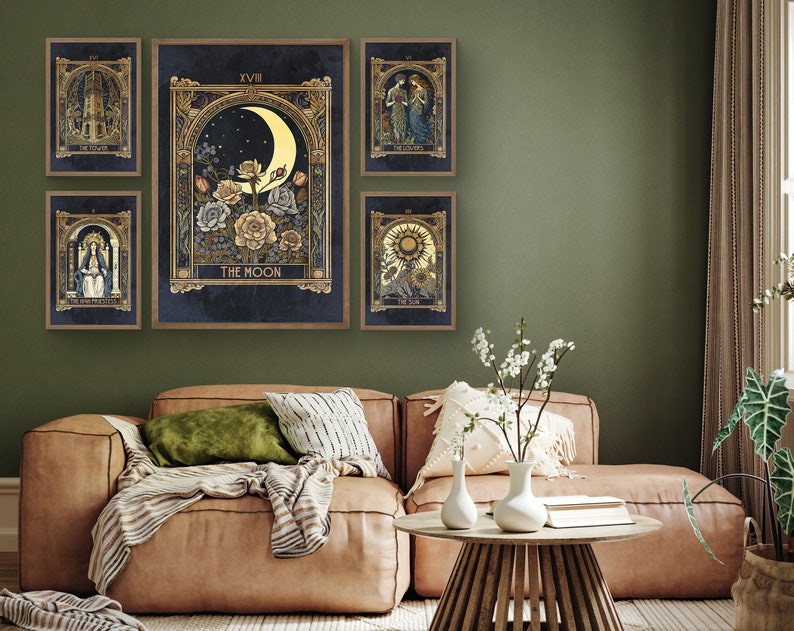May include: Five framed prints of tarot cards with gold accents and illustrations. The cards are The Tower, The Lovers, The Sun, The Moon, and The High Priestess. The prints are hanging on a green wall above a brown leather couch.