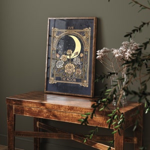 May include: A framed print of the The Moon tarot card with a crescent moon, stars, and flowers in gold and white on a dark blue background. The card number XVIII is in the top right corner.