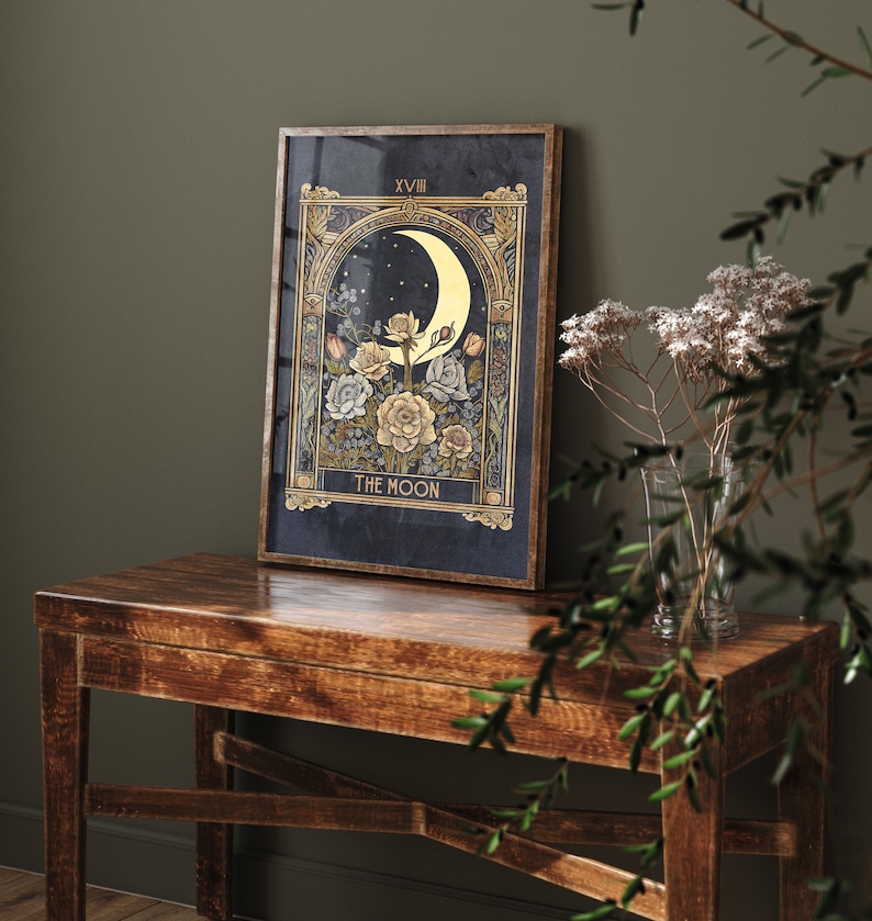 May include: A framed print of the The Moon tarot card with a crescent moon, stars, and flowers in gold and white on a dark blue background. The card number XVIII is in the top right corner.