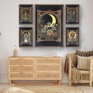 May include: Five tarot cards with gold accents and dark blue backgrounds. The cards are framed and displayed on a wall above a wooden dresser. The cards depict The Tower, The High Priestess, The Moon, The Lovers, and The Sun.