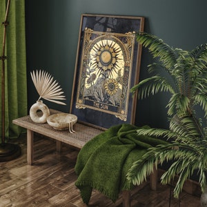 May include: A framed tarot card print with a gold and black design depicting the Sun card. The card is hanging on a dark green wall above a wooden bench with a green throw blanket. A potted plant with green leaves is in the corner of the image.