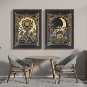 May include: Two framed prints with gold accents depicting tarot cards. The left print shows a sun with a face and rays, with the text "The Sun" below. The right print shows a crescent moon with a face and flowers, with the text "The Moon" below.