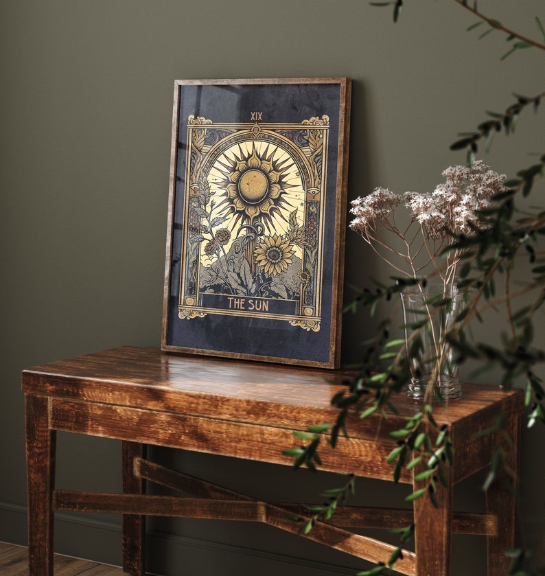 May include: A framed tarot card print with a gold and black design. The card depicts a sun with rays and sunflowers. The card is titled "The Sun" and numbered "XIX".