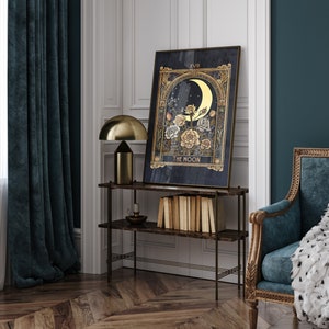 May include: A gold framed tarot card print with a dark blue background. The card depicts a crescent moon with a golden glow and a floral arrangement with white and yellow roses. The card is titled "The Moon" and is framed in a gold frame.