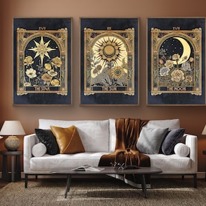 May include: Three framed prints with a dark blue background and gold accents. Each print features a celestial body, including a star, the sun, and the moon, surrounded by flowers. The text "The Star", "The Sun", and "The Moon" is printed below each image.