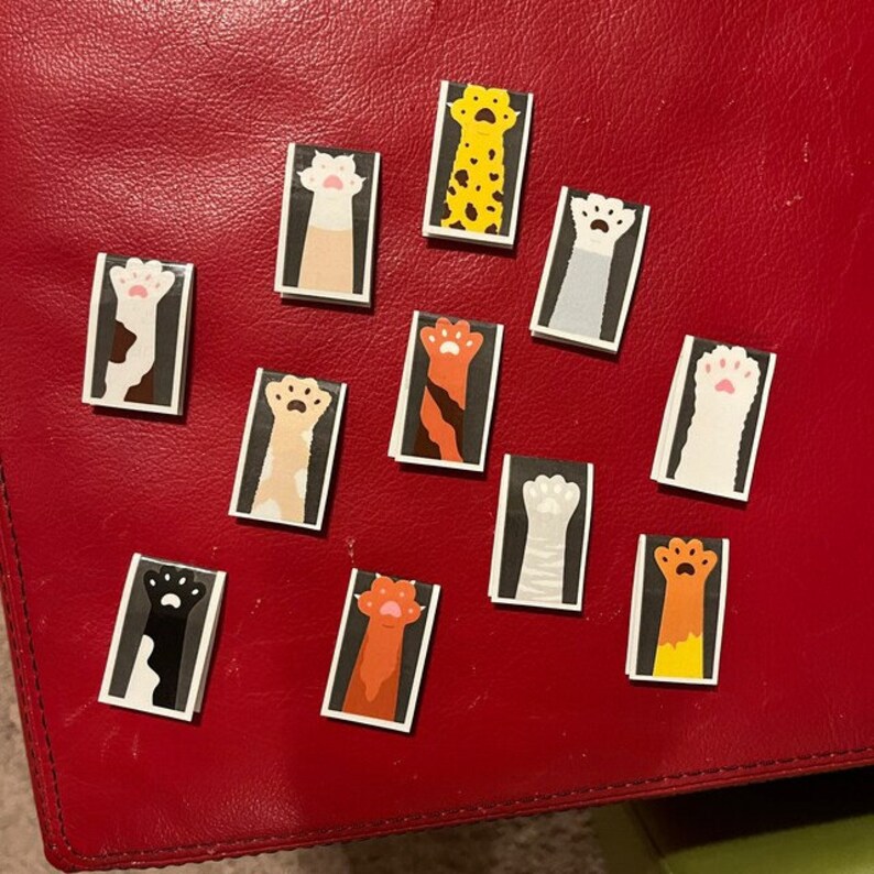 May include: Twelve colorful cat paw stickers with different colored fur patterns. The stickers are rectangular and feature a paw with claws raised in the air.