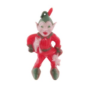 May include: A red plastic Christmas elf ornament with green pointed ears and a green hat. The elf is holding a white plastic toy in its right hand.
