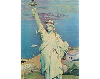 Peut inclure: Une carte postale représentant une photographie couleur de la Statue de la Liberté, une statue en cuivre vert d'une femme tenant une torche, debout sur Liberty Island dans le port de New York. La statue est vue d'en haut, avec l'eau et les terres environnantes visibles en arrière-plan.