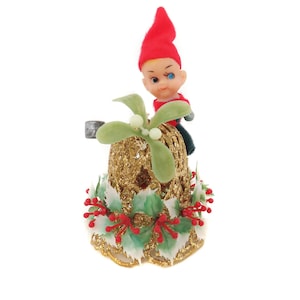 Könnte beinhalten: Eine goldene Glitzer-Weihnachtsglocke mit einem roten und grünen Stechpalmenkranz und einer kleinen Elfenfigur oben drauf.