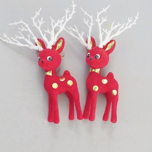 Op de afbeelding: Twee rode rendierornamenten met witte geweien en gouden accenten. Elk rendier heeft gouden stippen en een gouden kraag. Deze kerstversieringen in vintage-stijl zijn perfect om een feestelijke touch toe te voegen aan elke vakantiedisplay.