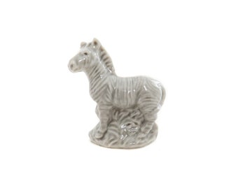 Könnte beinhalten: Eine graue Keramikfigur eines Zebras, das auf einem Sockel steht. Das Zebra hat schwarze Streifen und ist nach links gerichtet.