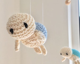 May include: A crocheted baby mobile with two white and blue turtle toys hanging from a wooden dowel.