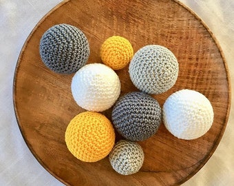 May include: A collection of crocheted balls in various colors, including gray, white, and yellow, arranged on a wooden surface.