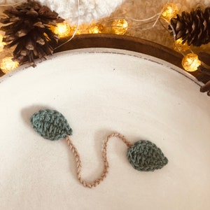 Könnte beinhalten: Ein grünes, gehäkeltes Blatt Lesezeichen mit einer gehäkelten Schnur in beige, die zwei Blätter verbindet.