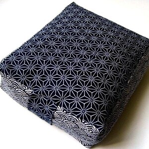 Könnte beinhalten: Quadratisches Kissen mit einem geometrischen Sternmuster in Marineblau und Weiß. Die Kanten weisen ein weißes Wellenmuster auf. Das Kissen hat eine quadratische Form, ideal zum Sitzen oder Dekorieren.