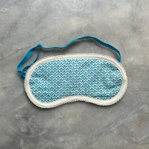 Könnte beinhalten: Eine blaue und weiße gemusterte Schlafmaske mit weißer Spitzenborte und einem blauen Gummiband.