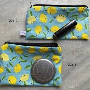 Könnte beinhalten: Zwei blaue Reißverschlusstaschen mit einem Zitronen-Druckmuster. Die obere Tasche ist 20 Zoll mal 10 Zoll groß und enthält einen schwarzen Lippenstift. Die untere Tasche ist 20 Zoll mal 13 Zoll groß und enthält einen runden silbernen Behälter.