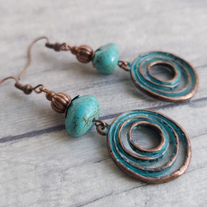 copper tone earrings with round pumpkin beads, star shaped bead caps, and turquoise aqua blue gemstone nuggets attached to charms of copper tone concentric circles with a verdigris patina on the surface, this colour is the same as the gemstones.