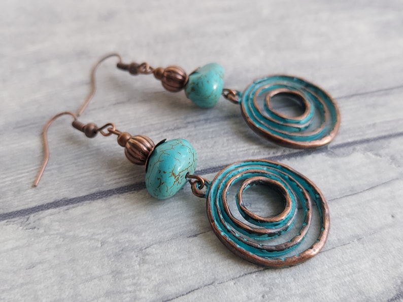 copper tone earrings with round pumpkin beads, star shaped bead caps, and turquoise aqua blue gemstone nuggets attached to charms of copper tone concentric circles with a verdigris patina on the surface, this colour is the same as the gemstones.