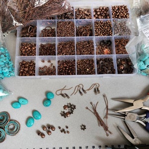 a flat lay out of work in progress making the earrings, a box with the various components that the earrings are made from, the gemstones and and the tools used to make them.