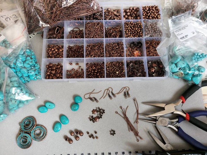 a flat lay out of work in progress making the earrings, a box with the various components that the earrings are made from, the gemstones and and the tools used to make them.
