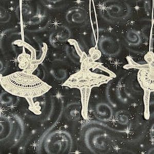 Op de afbeelding: Vier witte ballerina-versieringen van kant met een ophanglus. De ballerina's staan in verschillende poses en zijn gemaakt van delicate witte kant.