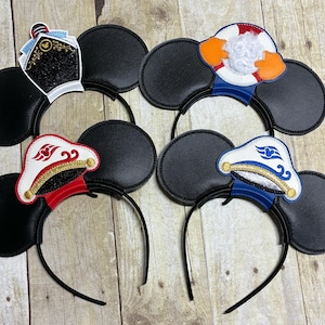 May include: Four black mouse ear headbands with themed designs. One features a black captain's hat with gold accents, another a life preserver, and two with white captain hats with red and blue accents.