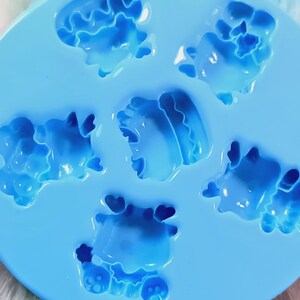 May include: A blue silicone mold with six cavities shaped like cartoon animals. The mold is designed for making small, decorative items.
