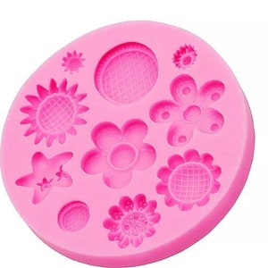 Puede incluir: Molde de silicona rosa con ocho formas diferentes de flores y estrellas. El molde está diseñado para hacer decoraciones de fondant o pasta de goma.