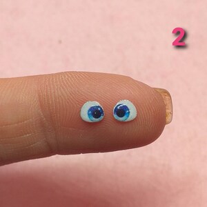 Könnte beinhalten: Zwei blaue Puppenaugen mit weißer Sklera, auf einem Finger.