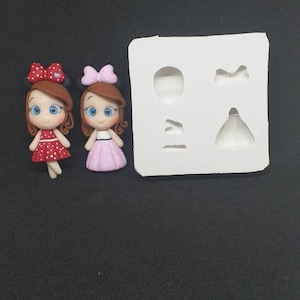 May include: Two small, hand-painted doll figures with brown hair, blue eyes, and polka dot dresses. The dolls are in a white silicone mold with four cavities, including a bow, a dress, and a head.