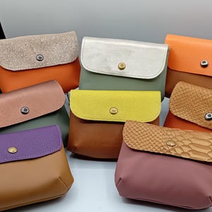 Peut inclure: Assortiment de neuf petits portefeuilles en cuir de différentes couleurs et textures. Les portefeuilles ont une fermeture à rabat avec un bouton en métal.