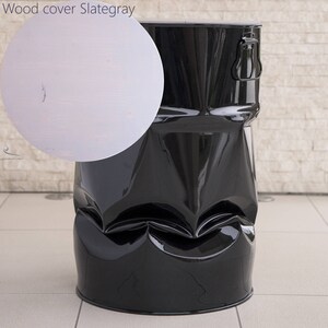 May include: A glossy black metal drum-shaped stool with a unique, textured design. The stool has a shiny finish and a sturdy appearance. A circular inset shows a wood cover in Slate Gray.