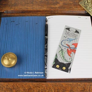Blue Dragon Notebook, featuring my original pen and ink dragon illustration, inside cover open and ready to write in, shown with bookmark and vintage Victorian writing desk accessories. Made in the UK. Design and illustration © Nicola L Robinson | Teeth and Claws