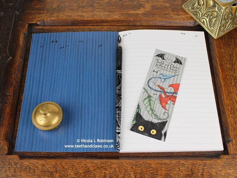 Blue Dragon Notebook, featuring my original pen and ink dragon illustration, inside cover open and ready to write in, shown with bookmark and vintage Victorian writing desk accessories. Made in the UK. Design and illustration © Nicola L Robinson | Teeth and Claws