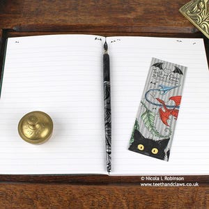 Gothic Crows Notebook, featuring my original pen and ink crow illustration, open flat showing lined pages, with bookmark and vintage Victorian writing desk accessories. Made in the UK. Design and illustration © Nicola L Robinson | Teeth and Claws