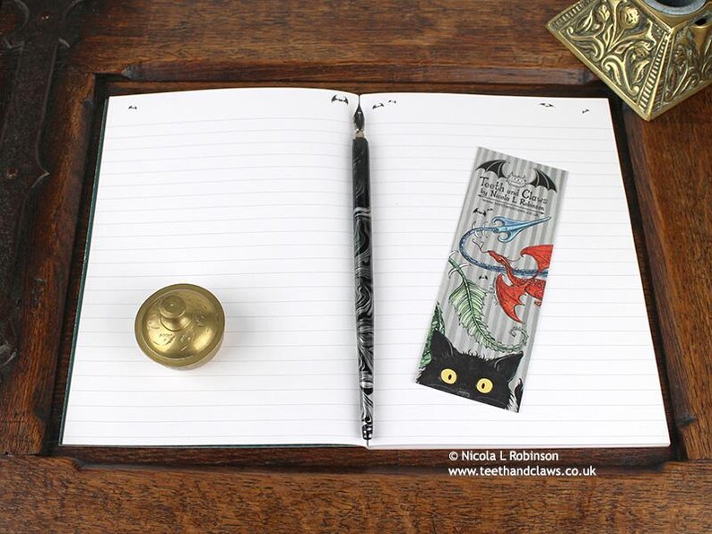 Gothic Crows Notebook, featuring my original pen and ink crow illustration, open flat showing lined pages, with bookmark and vintage Victorian writing desk accessories. Made in the UK. Design and illustration © Nicola L Robinson | Teeth and Claws