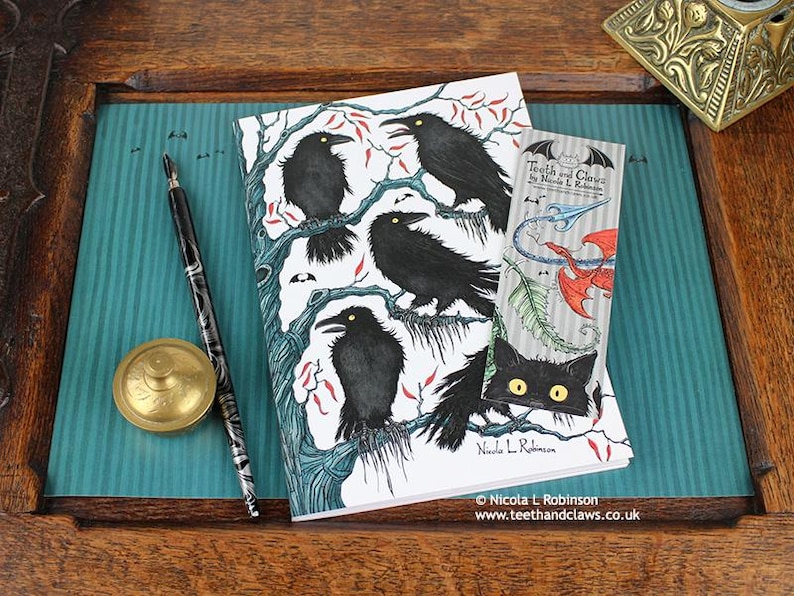 Gothic Crows Notebook featuring my original pen and ink crow illustration, front cover, shown with bookmark and vintage Victorian writing desk accessories. Made in the UK. Design and illustration © Nicola L Robinson | Teeth and Claws
