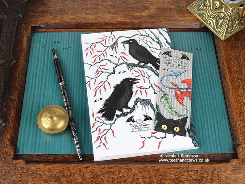 Gothic Crows Notebook featuring my original pen and ink crow illustration, back cover, shown with bookmark and vintage Victorian writing desk accessories. Made in the UK. Design and illustration © Nicola L Robinson | Teeth and Claws