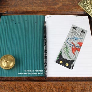 Gothic Crows Notebook, featuring my original pen and ink crow illustration, inside cover open and ready to write in, shown with bookmark and vintage Victorian writing desk accessories. Made in the UK. Design and illustration © Nicola L Robinson | Teeth and Claws