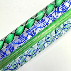 May include: Close-up of four glass rods with decorative patterns. The rods feature green, blue, and clear glass with designs including spirals, intersecting lines, and floral motifs. The rods are angled, showcasing the variety of patterns.