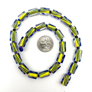May include: A necklace of rectangular glass beads with yellow and blue stripes. The beads are strung together with small black and blue spacer beads. A coin is included for size reference. The beads are on a white background.