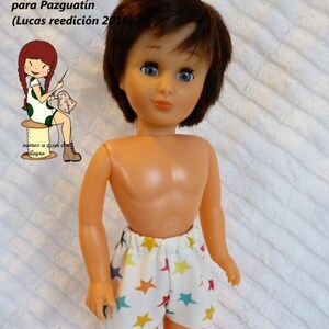 May include: A doll with brown hair and blue eyes wearing white shorts patterned with colourful stars. The image includes Spanish text: "Tutorial y patrones un calzón para Pazguatín (Lucas reedición 2018)" and the word "anilegra".